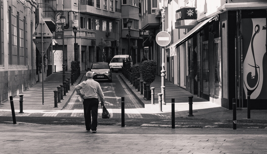 A man walking away down a street in Alicante, black and white