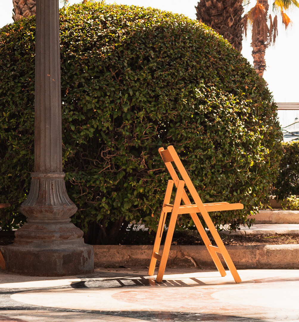 A single orange plastic chair against a weathered wall in Alicante