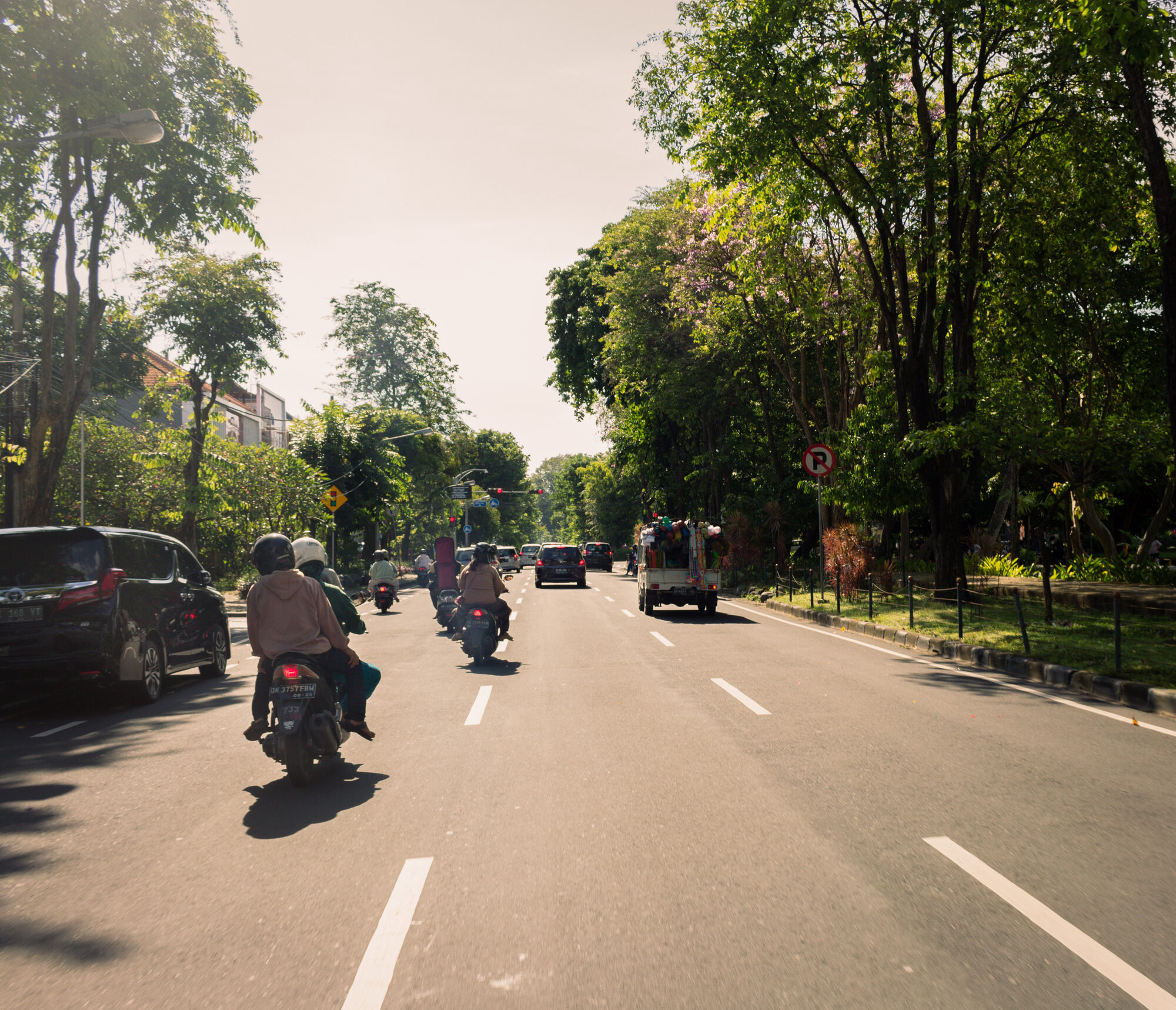 Motorbikes and cars on a tree-lined street in Bali