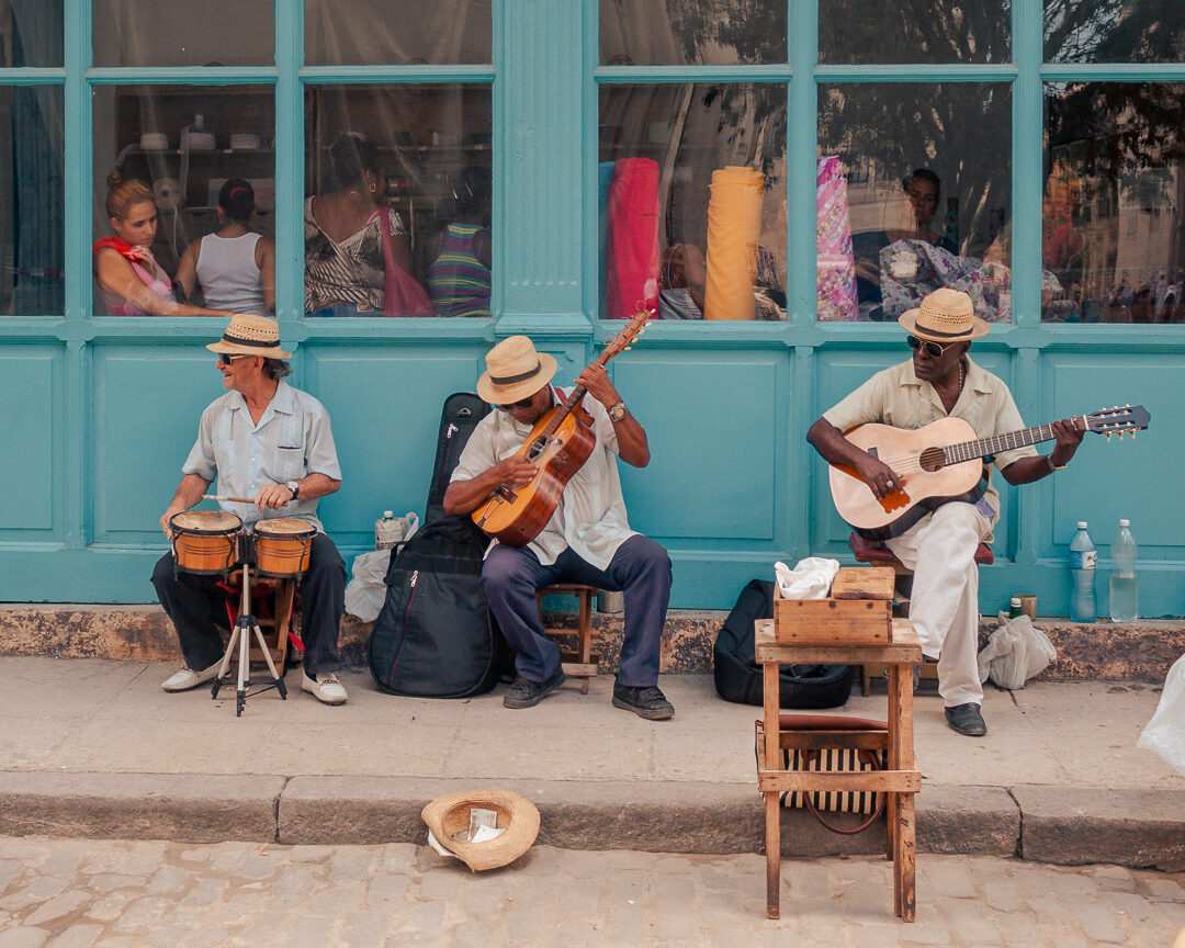 Street musicians playing guitar and bongos against a turquoise storefront in Havana