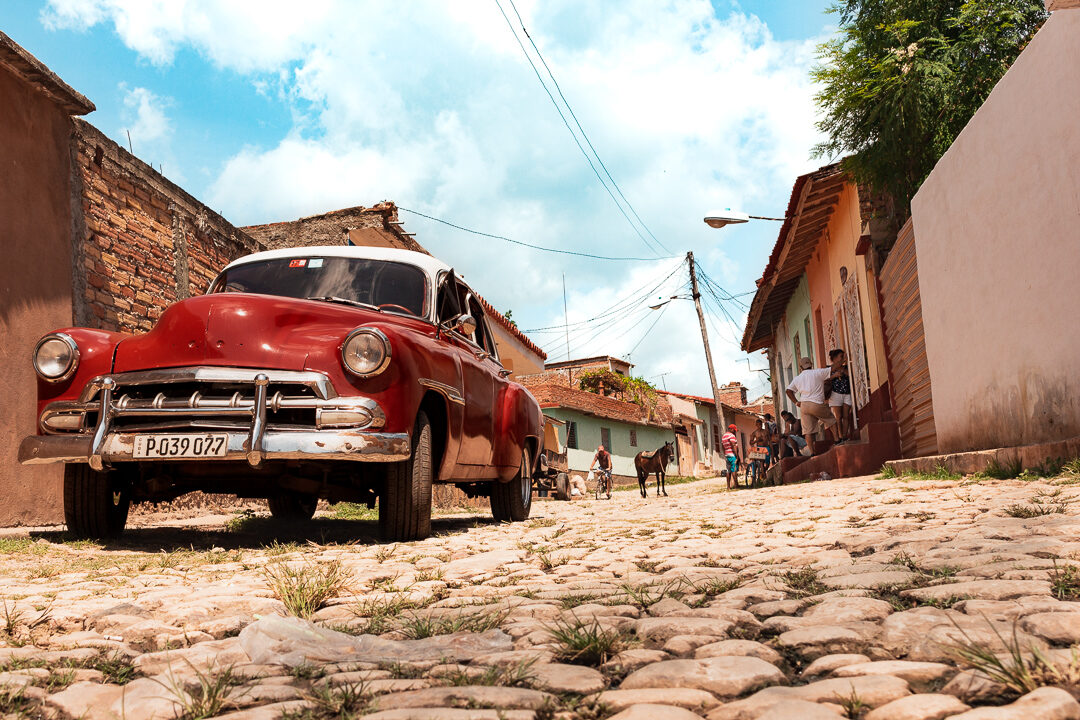 A red vintage car parked on a cobblestone street in Trinidad